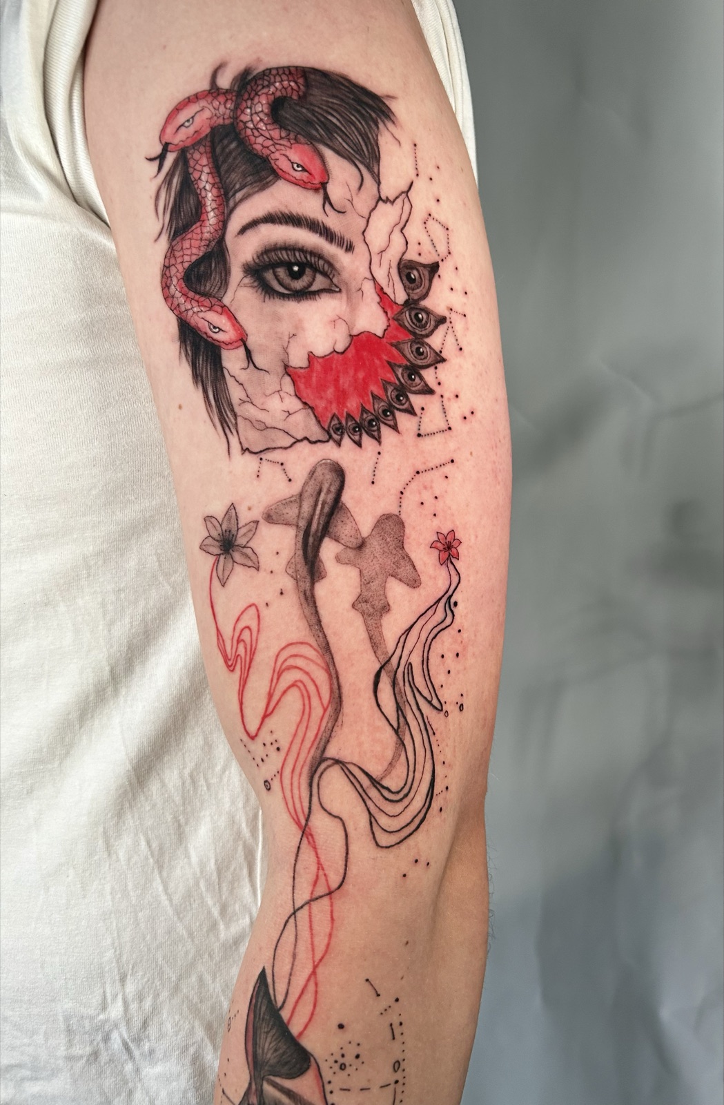 Black, grey and red arm tattoo — a woman's face with a red snake, an eye and abstract red linework